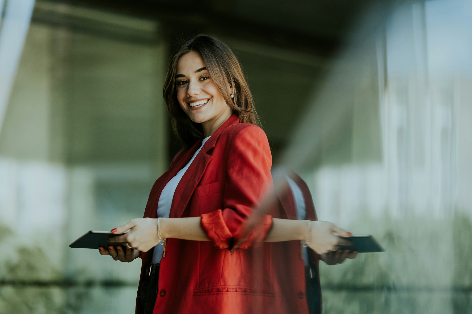 Confident businesswoman in red blazer outside glass office building at dusk